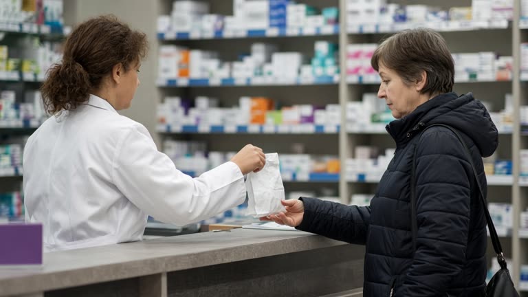 Retail pharmacy counter with pharmacist in white coat handing a paper bag to a customer, shelves of boxed medicine blurred behind, bright store lighting, no readable labels