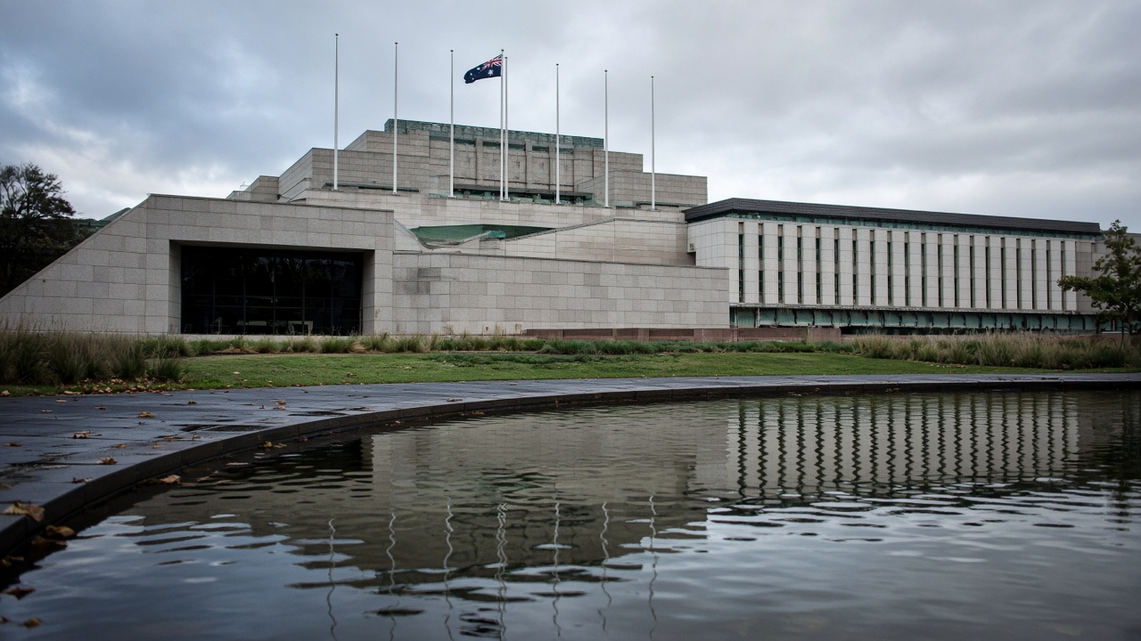 Parliament House Canberra reflected in a small ornamental pool on a windy spring morning, flagpoles and granite facade, no readable text on buildings