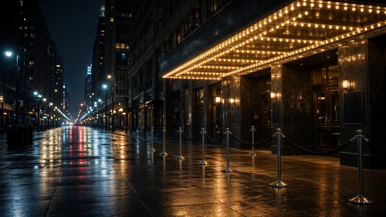 Theater district street at night with illuminated marquee bulbs and empty ticket queue stanchions, wet pavement reflections, no faces, no logos or readable text