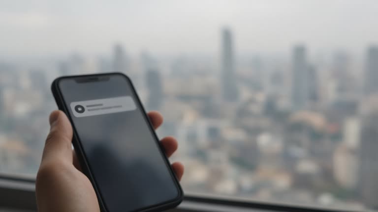 Hand holding smartphone with blurred notification screen against hazy city skyline from high window, no readable text, no faces