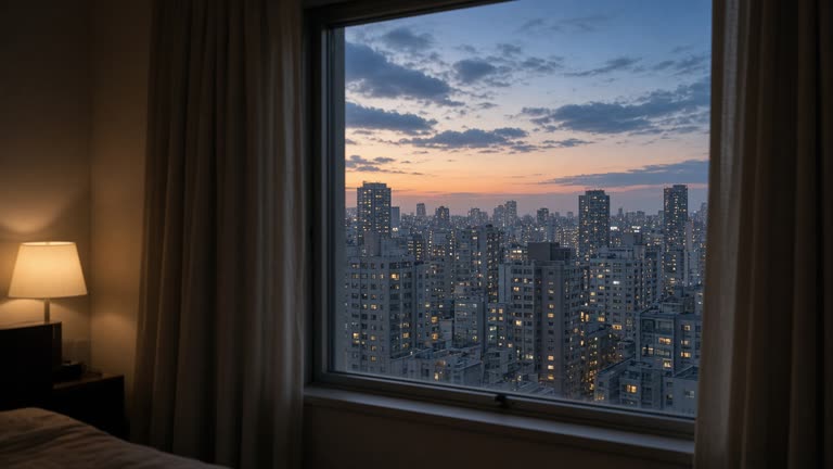 Hotel room window view of distant Tokyo apartment towers at dusk with soft interior lamp light, curtains half open, no logos or readable text