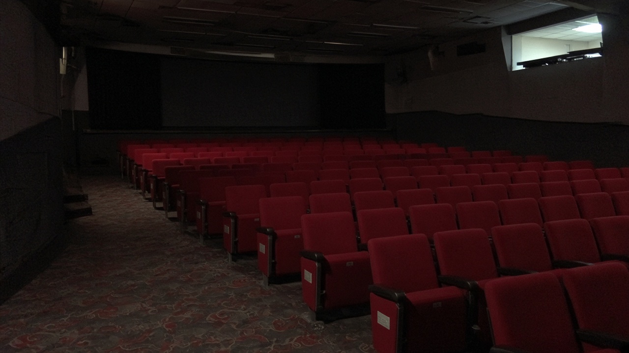 Empty cinema auditorium with red seats and light from projection booth, carpet aisle, no logos or readable text.