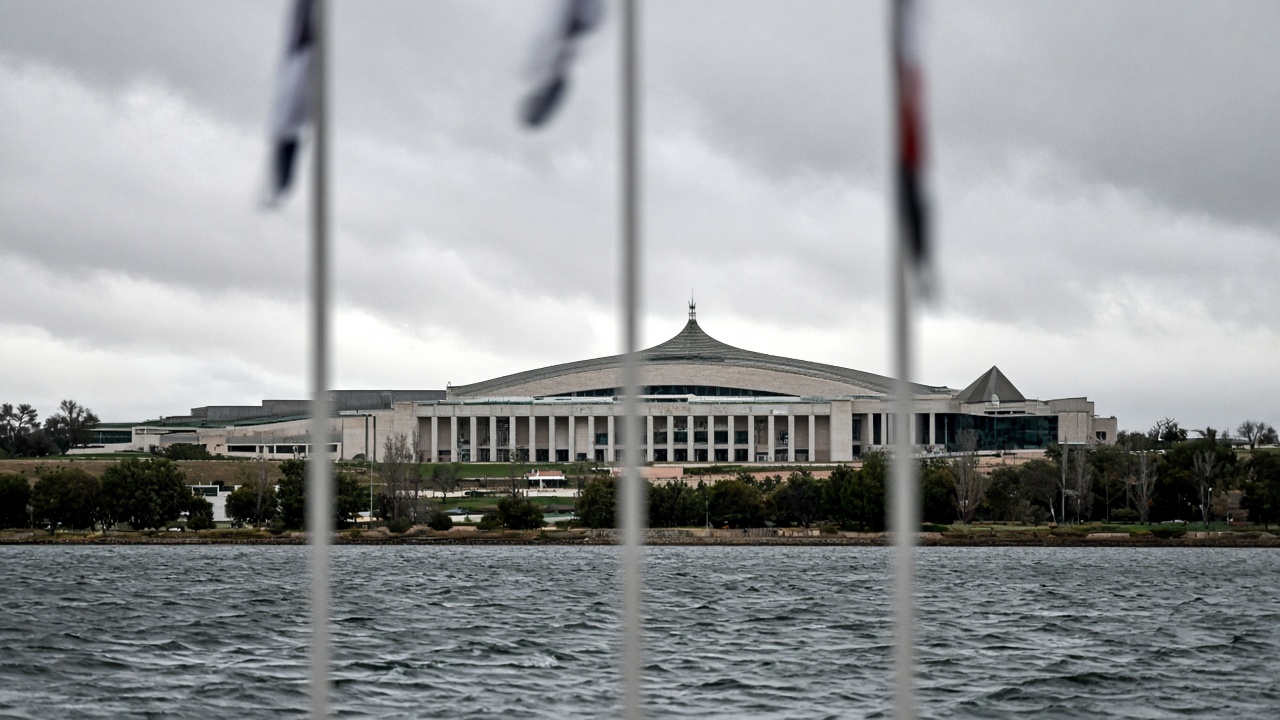 Canberra Parliament House viewed across Lake Burley Griffin on a windy overcast morning, flagpoles with flags blurred, no readable text on buildings