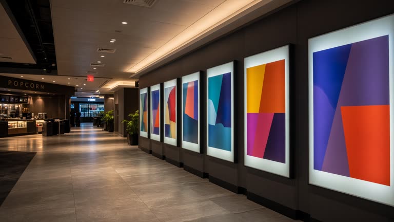 Multiplex cinema lobby with poster lightboxes showing abstract colour blocks without readable titles, evening interior lighting, no people facing camera