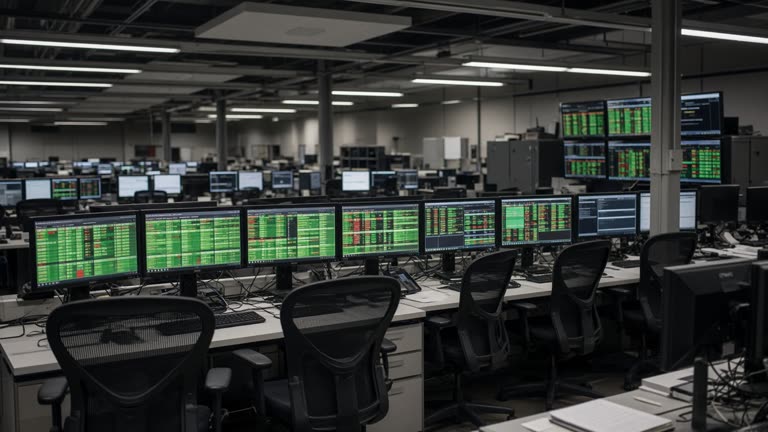 Retail brokerage trading floor with rows of desktop monitors showing green and red price tiles, fluorescent light, empty chairs, no logos or readable text