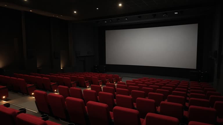 UK multiplex auditorium with red seats and blank screen before a showing, dim aisle lighting, no studio logos on screen