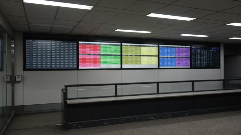 Empty Tokyo stock exchange gallery with large electronic quote boards showing colored price blocks, fluorescent ceiling light, slight grain, no readable numbers or logos