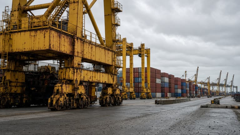 Industrial container terminal with yellow cranes and stacked shipping containers under overcast daylight, rust streaks on metal, documentary wide angle, no logos or readable text